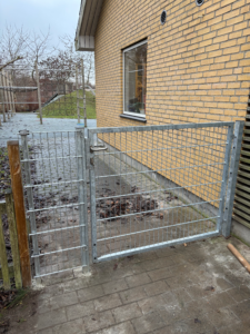 Galvaniseret panelhegn monteret langs bygning med integreret låge